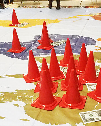 Eine Welt Programm Bild: Weltkarte mit Pylonen und Dollarnoten im Club Orange