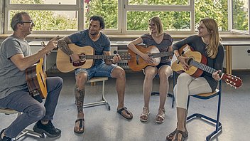 Bild: Eine fröhliche Gruppe erlernt gemeinsam das Gitarrenspielen