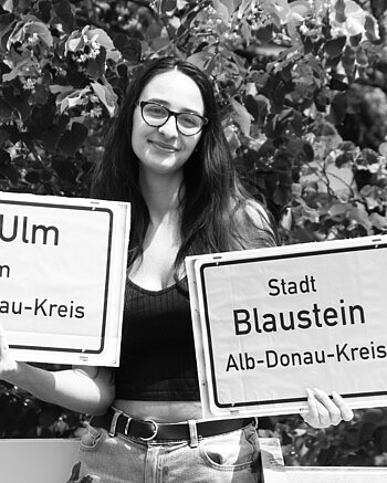 vh Ulm in Blaustein Bild: Frau hält Stadtschild Blaustein und Schild vh Ulm im Alb-Donau-Kreis