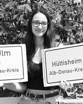 Vh Ulm in Hüttisheim Bild: Frau hält Ortsschild Hüttisheim und Schild vh Ulm im Alb-Donau-Kreis